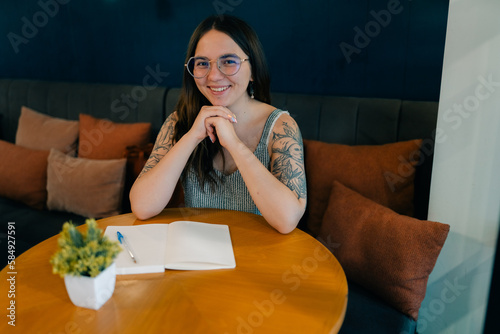 Gorgeous Caucasian hipster young woman in glasses plans her day in a notebook