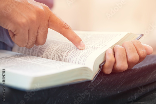 Closeup of Man finger pointing text in a bible. Man reading a bible or book with sunlight.