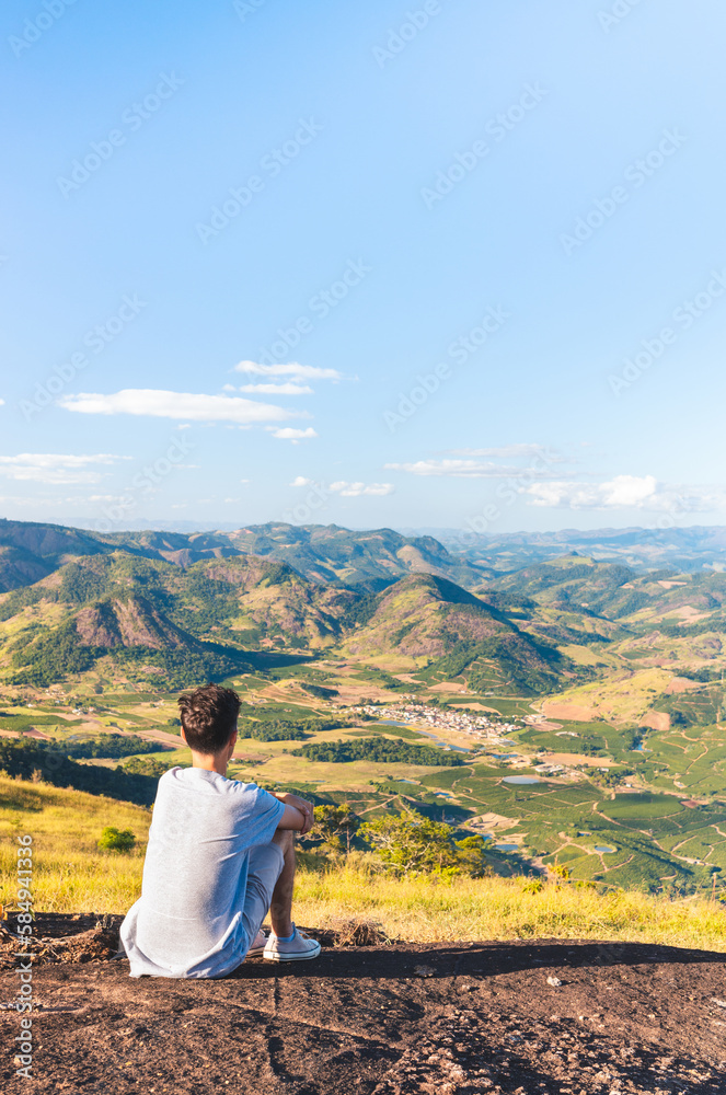 Man feeling good and calm sitting on top of a mountain while looking at the beautiful landscape of the valley. Person having thoughts and reflections while resting.
