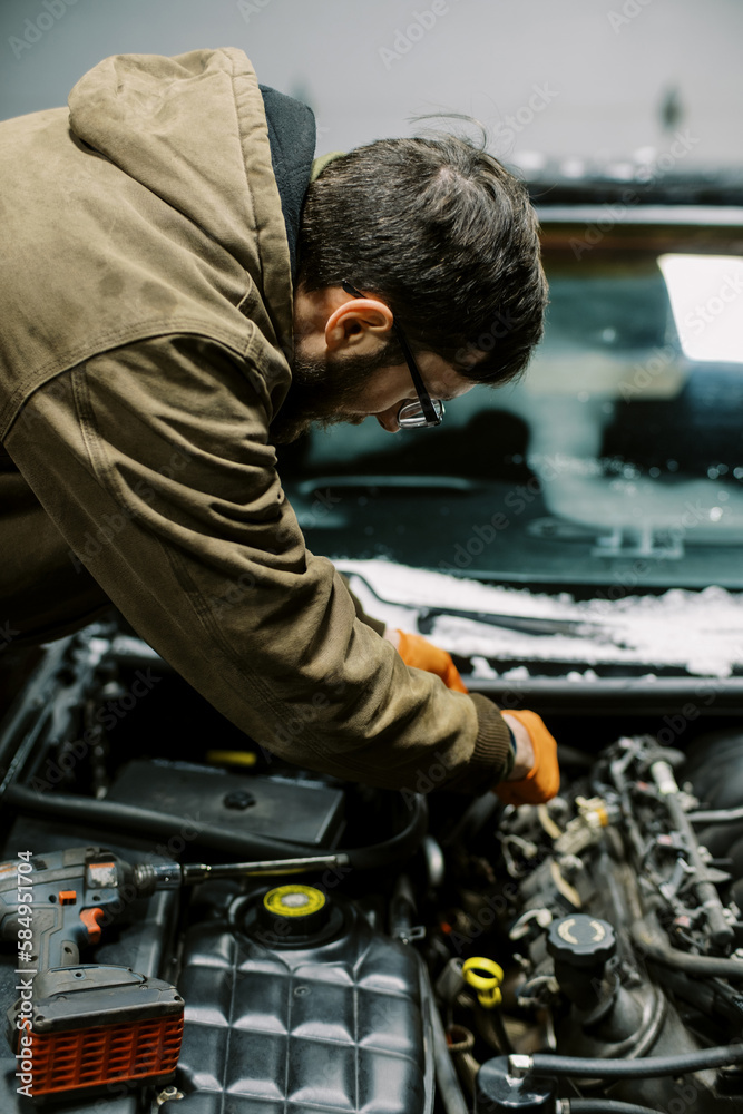 Young man standing in his garage while working on a car Young man standing in his garage while working on a car