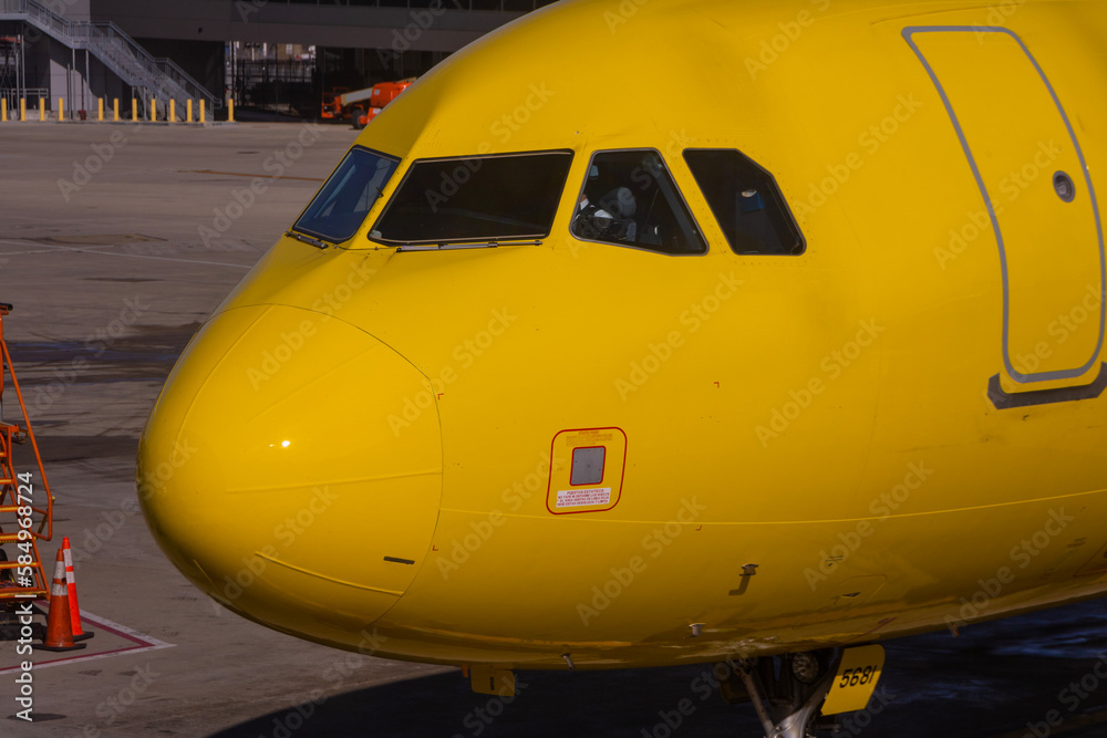 Obraz premium A close up image of a bright yellow airplane waiting on the tarmac at an airport with a pilot sitting inside of the cockpit of the jet.