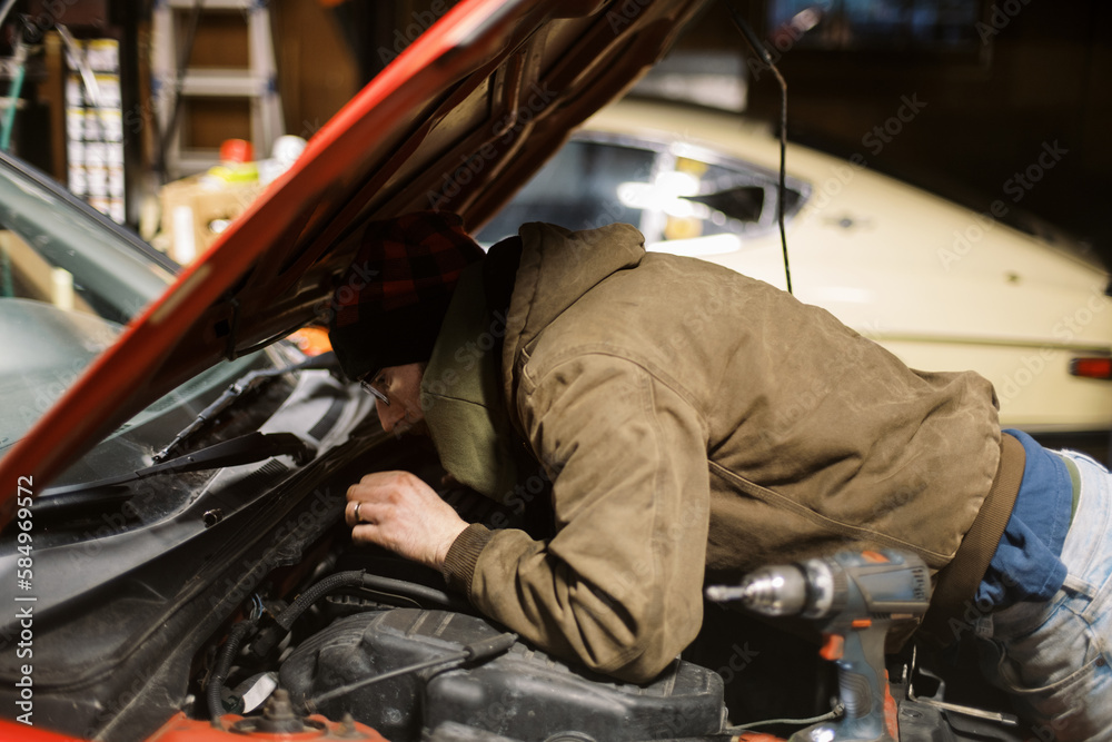Millennial Mechanic working on a red car in workshop Millennial Mechanic working on a red car in workshop