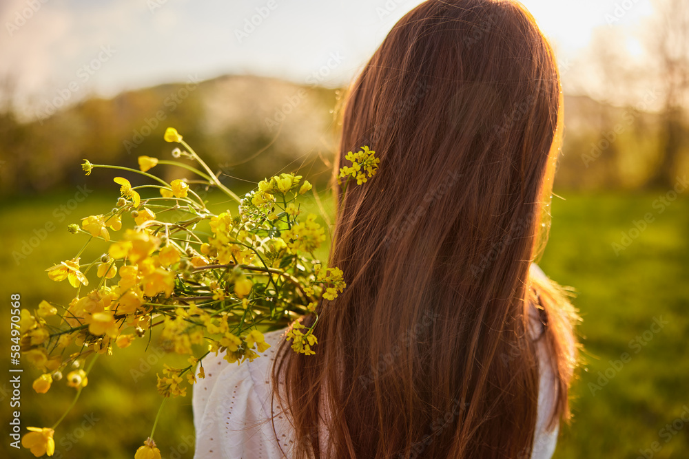 Naklejka premium photo from the back of a red-haired woman with a bouquet of flowers in the rays of the setting sun