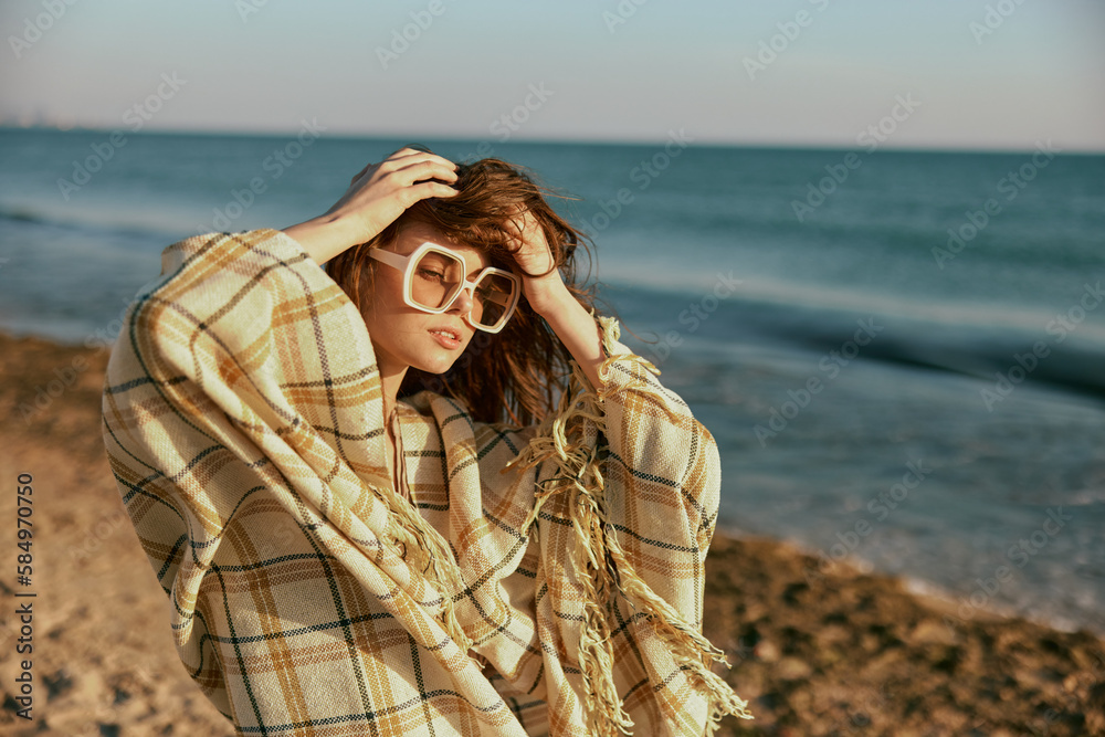 portrait of a woman in large glasses, wrapped in a blanket on the sea coast, holding her hair in the wind