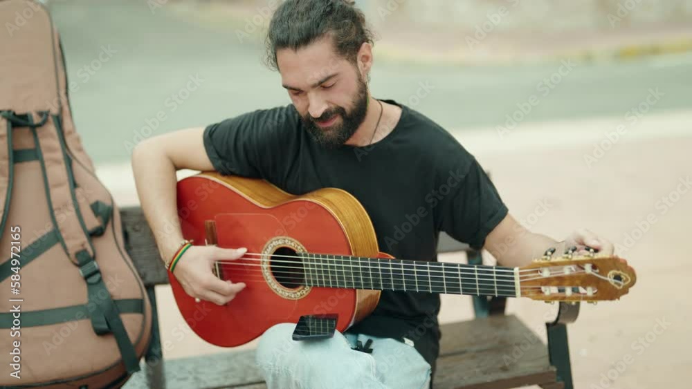 Young hispanic man musician playing classical guitar sitting on bench at street