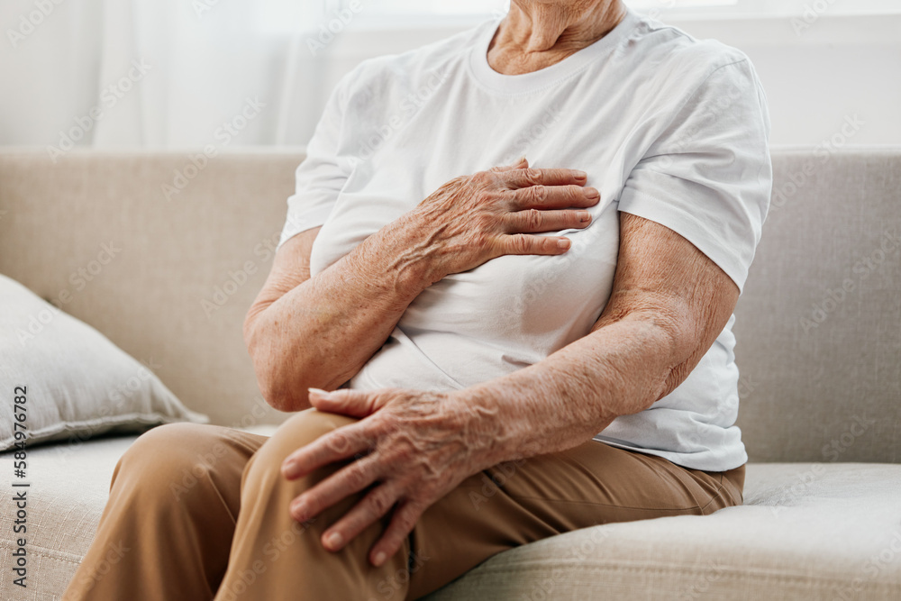 Elderly woman severe chest pain sitting on the sofa, health problems in