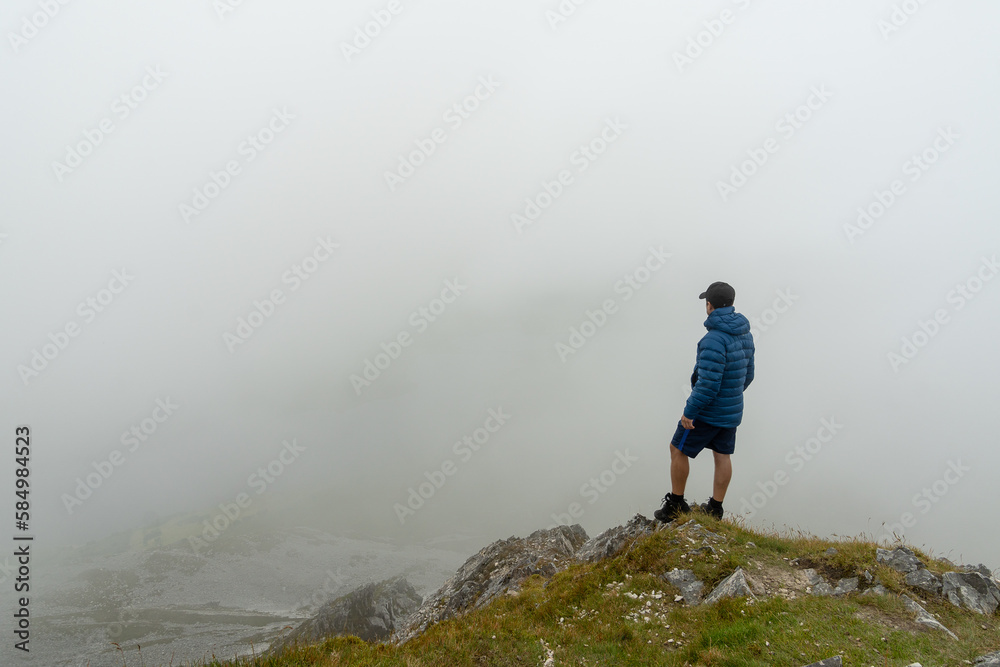 Man standing on top of mountain admiring landscape with fog