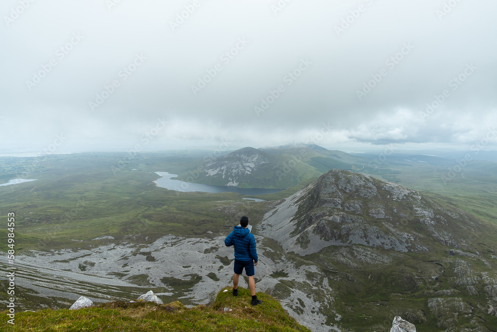 Man standing on top of mountain admiring landscape of Errigal mountain Man standing on top of mountain admiring landscape of Errigal mountain