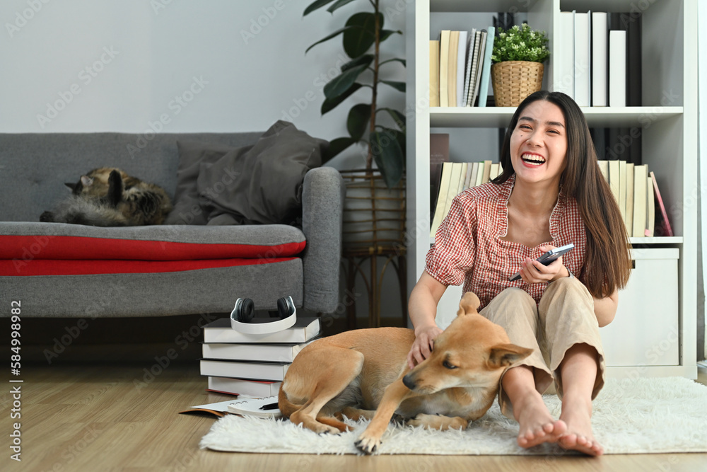 Happy young pretty woman in casual clothes spending time with lovely dog in bright living room