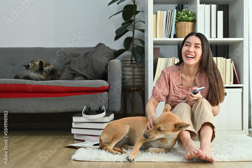 Happy young pretty woman in casual clothes spending time with lovely dog in bright living room © Prathankarnpap