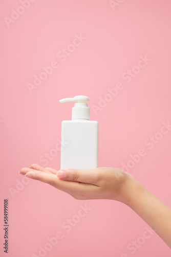 An elegant hand model with a pump bottle dispenser placed on over pink pastel background. Beauty cosmetic product for skin care concept. Mockup