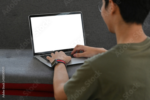 Back view of young man in casual clothes sitting in living room and using laptop computer.