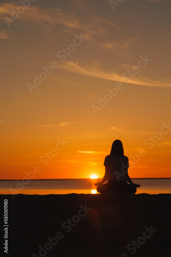 yoga meditation, silhouette of woman at sunset in lotus position. health recreation and sports, outdoor training. poster, postcard. person is engaged in breathing practices on seashore. mental health © MyJuly