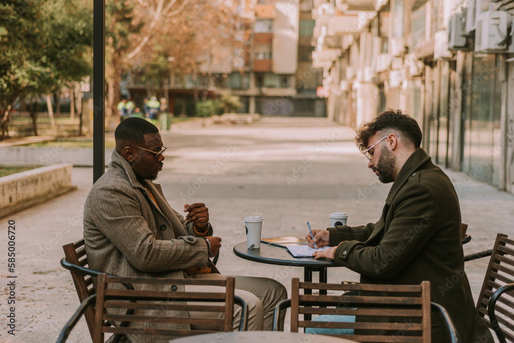 Fototapeta premium Young executive ceo manager writing notes in the notebook and explaining them to his black male partner