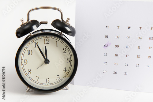 White calendar with marked date 8 March and black retro alarm clock on white background using as year plan. International Women's Day reminder, special event day concept. Time and calendar concept