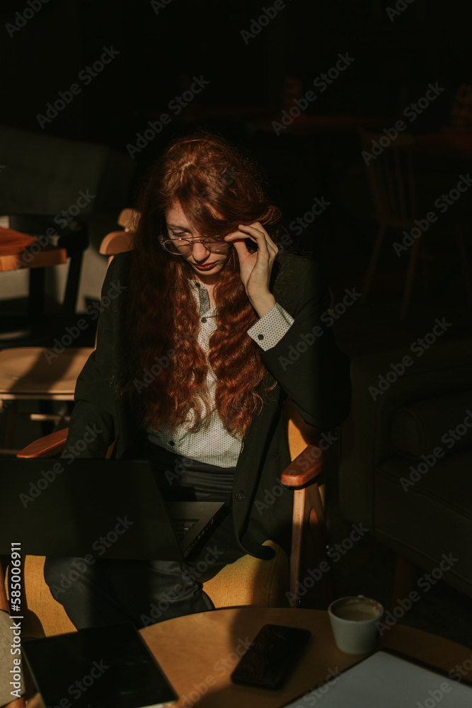 A close up shot of lovely ginger female person putting eyeglasses to start working on the lap top. Remote work from coffee bar