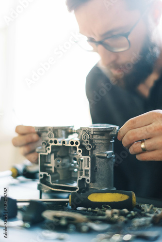 Millennial Man assembling carburetor on kitchen table in his home 