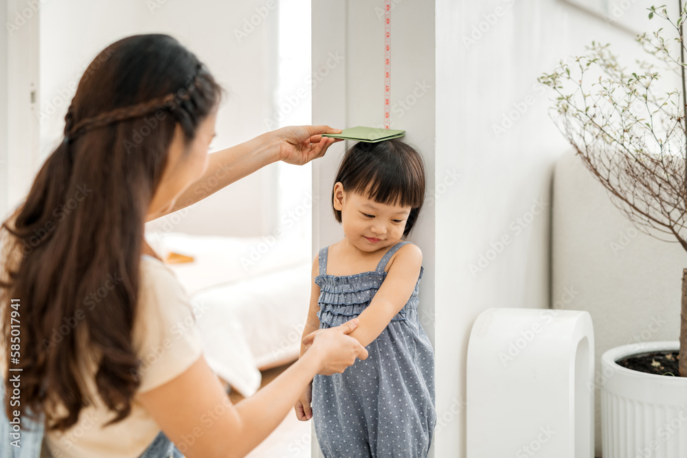Happy Asian mother using book to measure height of little girl Happy Asian mother using book to measure height of little girl