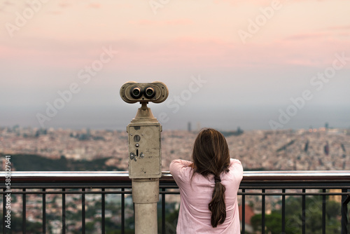 Female kid next to binoculars looking at the city photo