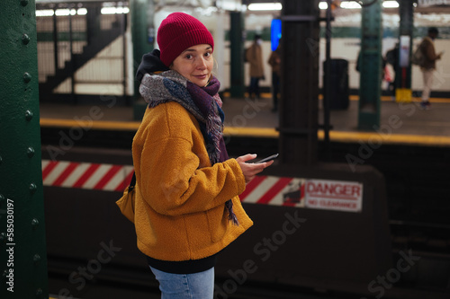 Young female wearing red hat and yellow jacket waits for the train