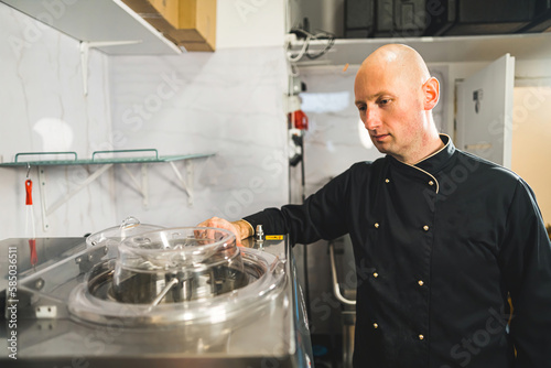Man wearing black chef uniform standing near ice cream pasteurizer in a production kitchen. High quality photo