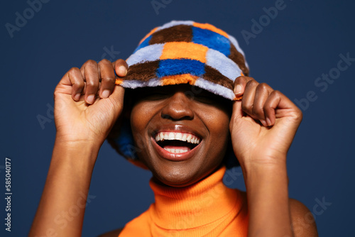 Happy woman hiding eyes with hat against blue background