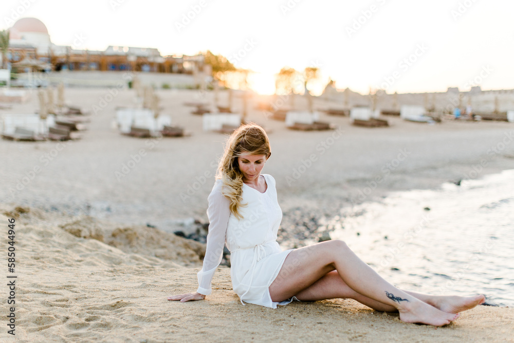 Frau im weißen Kleid sitzt am Strand