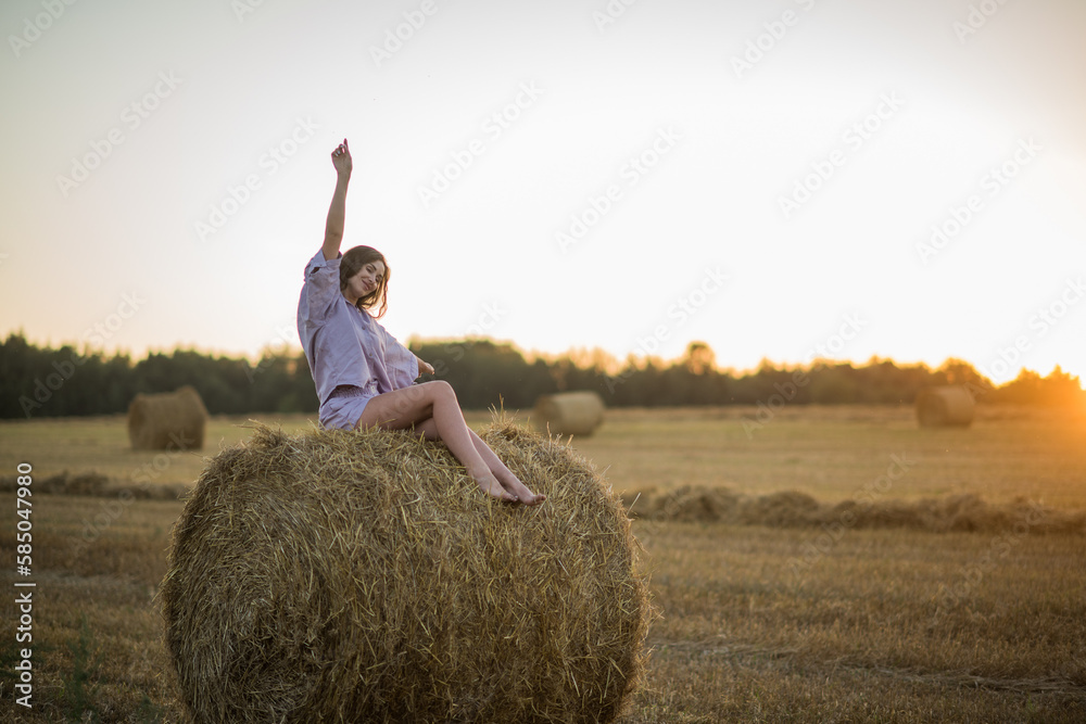 a happy girl with long hair sits on a haystack in a field at sunset and enjoys nature, loneliness and freedom. a happy girl with long hair sits on a haystack in a field at sunset and enjoys nature, loneliness and freedom.