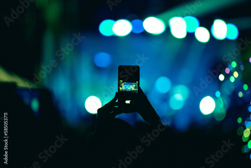 Person holding smartphone and silhouettes of concert crowd with stage lights