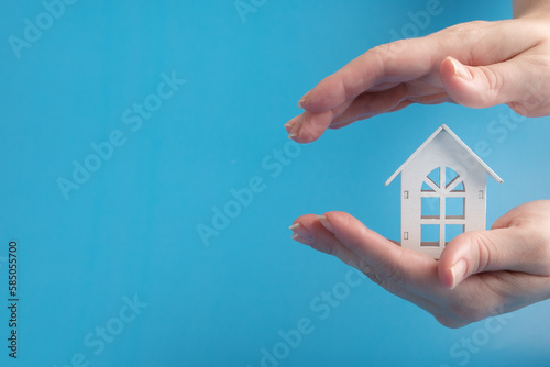 property insurance, real estate security, home protection, house is covered by female hands, blue background, copy space