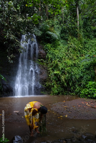Photo A tahitian woman doing a purification act in the water in a small pond of a scenic waterfall