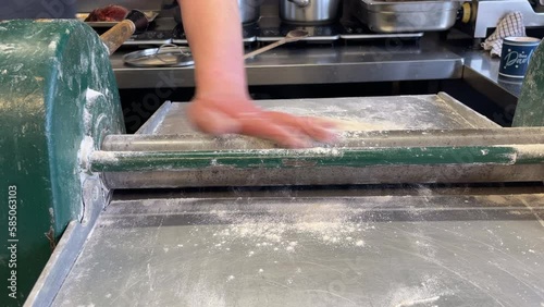 The chef rolls pastry with an old pastry machine in the kitchen front view 