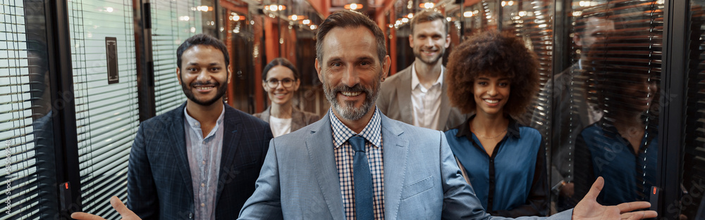 Group of happy, motivated business people standing together at office with their leader Group of happy, motivated business people standing together at office with their leader