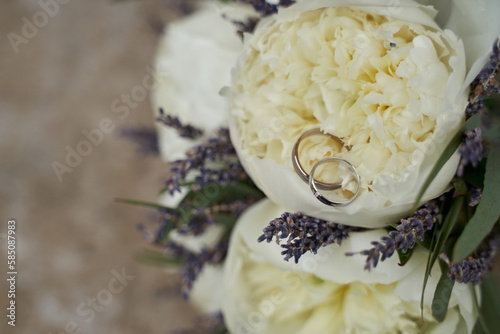 delicate wedding bouquet of large white peonies and lavender and white gold wedding rings on it