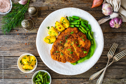 Breaded fried pork chop with green beans and potatoes on wooden table 