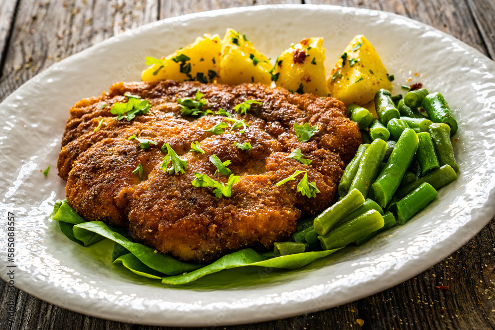 Breaded fried pork chop with green beans and potatoes on wooden table
