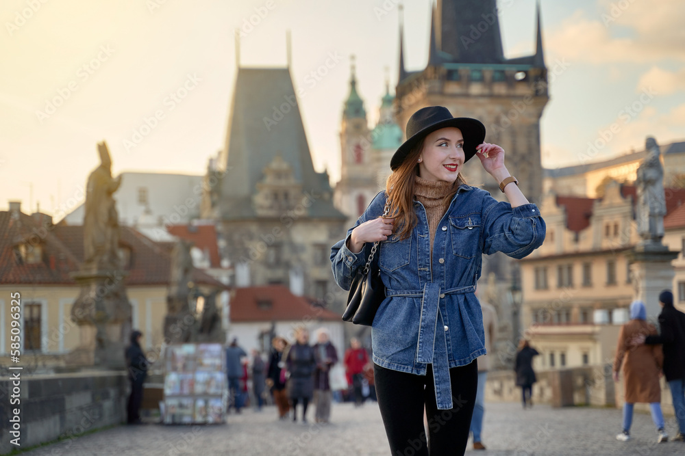 Female traveller tourist on the Charles Bridge in Prague, Czezh Repubic. Stylish beautiful young woman earing black hat. Elegant retro lady fine art portrait.