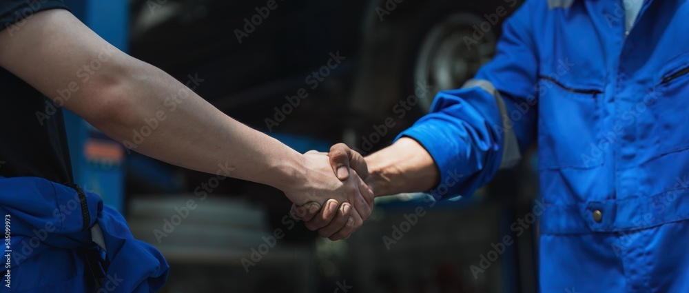 Young man client shaking hands with auto mechanic in red uniform having a deal at the car service