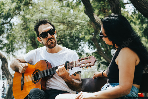 Photo of couple singing a song with acoustic guitar on a sunny day. Lifestyle, music and couples concept.