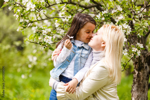 Happy woman and child in the blooming spring garden. Mothers day holiday concept.