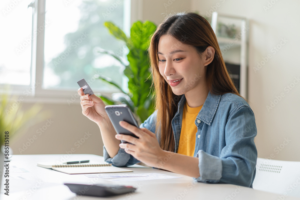Close up view hands of young woman holding a credit card and doing bank transactions via mobile phone application at home Close up view hands of young woman holding a credit card and doing bank transactions via mobile phone application at home