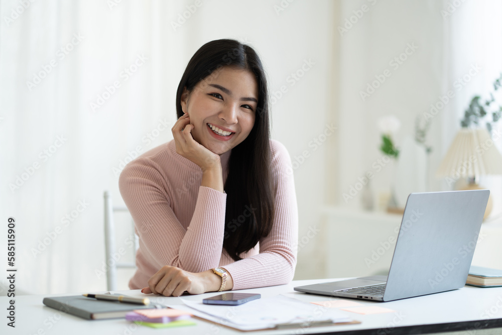 Portrait of young attractive Asian businesswoman smiling to the camera while sitting at her desk. Portrait of young attractive Asian businesswoman smiling to the camera while sitting at her desk.