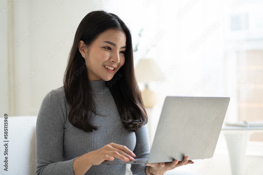 Young beautiful Asian woman using laptop computer while sitting on the sofa at her living room. Young beautiful Asian woman using laptop computer while sitting on the sofa at her living room.
