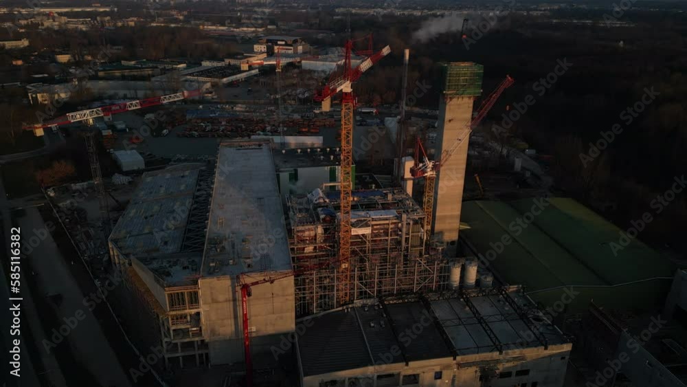 Drone circulating around chimney of the New Constructed Incineration Plant in Warsaw. Tower cranes against blue cloudy sky at the sunrise and industrial zone. Drone circulating around chimney of the New Constructed Incineration Plant in Warsaw. Tower cranes against blue cloudy sky at the sunrise and industrial zone.