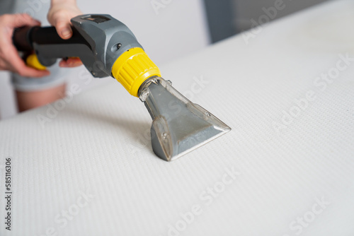 Wet and dry vacuum cleaner working on white bed mattress