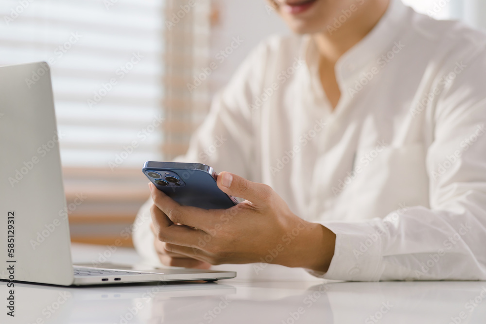 Cropped shot of millennial Asian businessman is working remotely from his home office with his smartphone. Cropped shot of millennial Asian businessman is working remotely from his home office with his smartphone.