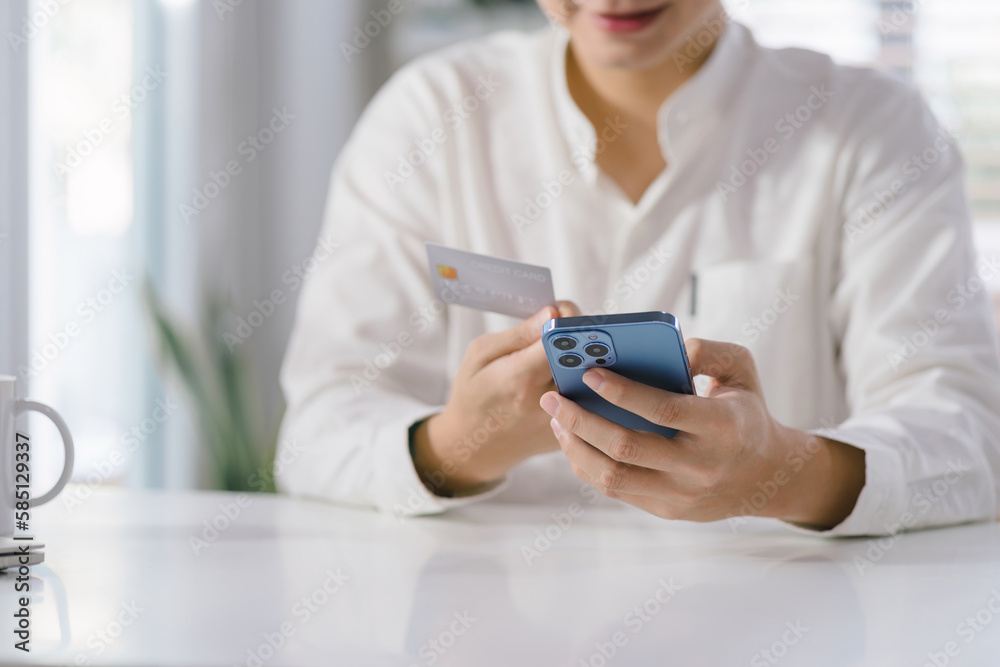 Cropped shot of millennial man is paying with a credit card online while placing orders via mobile internet and making transactions using a mobile banking application. Cropped shot of millennial man is paying with a credit card online while placing orders via mobile internet and making transactions using a mobile banking application.