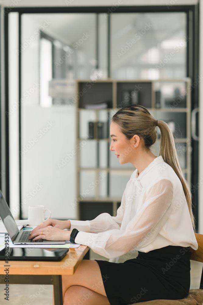 Tech-Savvy and Business-Savvy: A Young, Attractive Businesswoman Thrives in the Modern Office with Her Trusty Laptop. Tech-Savvy and Business-Savvy: A Young, Attractive Businesswoman Thrives in the Modern Office with Her Trusty Laptop.