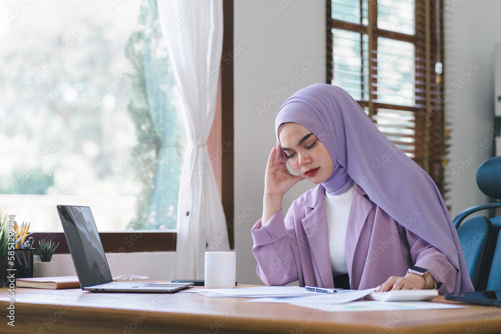 Stressed Muslim millennial businesswoman wearing a purple hijab working from home on laptop looking worried, tired and overwhelmed. Stressed Muslim millennial businesswoman wearing a purple hijab working from home on laptop looking worried, tired and overwhelmed.