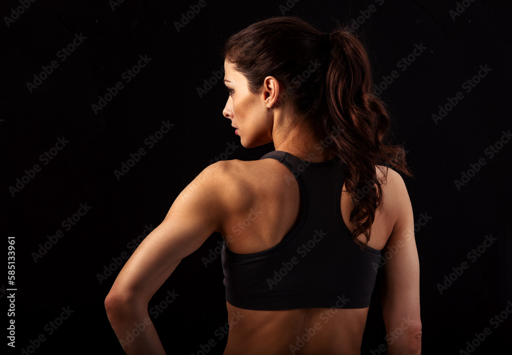 Serious female sporty muscular with ponytail doing stretching workout the shoulders, blades and arms in sport bra, standing on black background with empty space. Back view, profile face Serious female sporty muscular with ponytail doing stretching workout the shoulders, blades and arms in sport bra, standing on black background with empty space. Back view, profile face